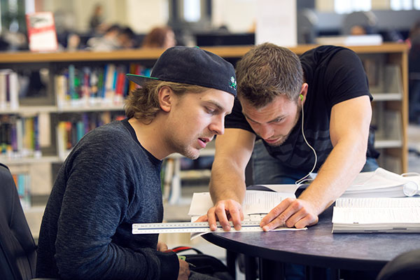 Two male students work on a project together in the Library.